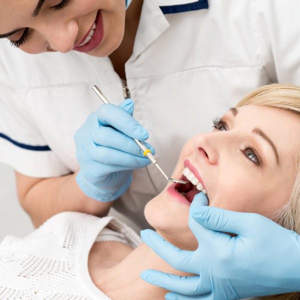 Female dentist examining teeth using mirror in clinic